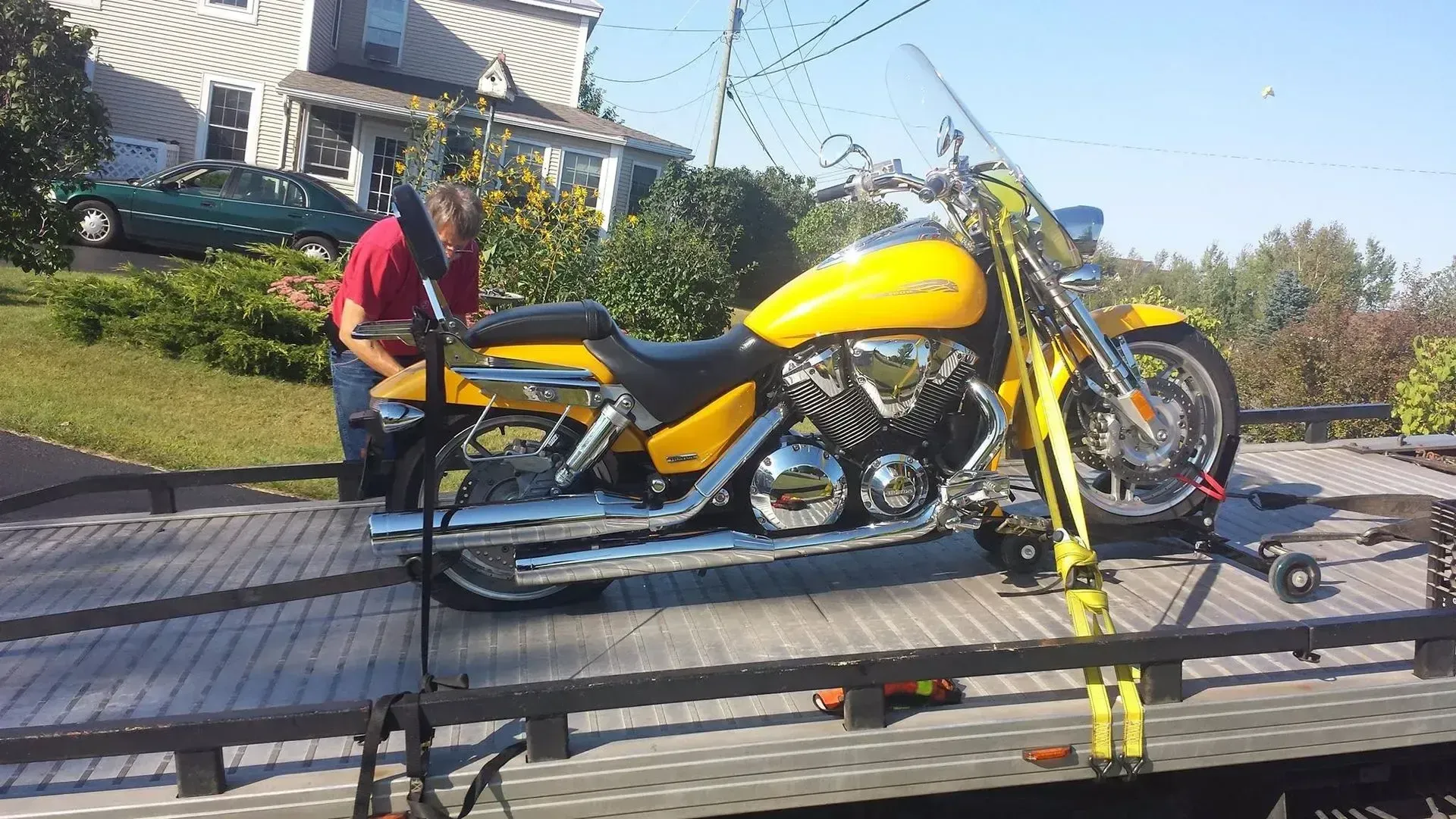 A man is standing next to a yellow motorcycle on a trailer