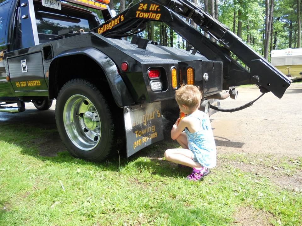 A little girl is kneeling next to a tow truck.