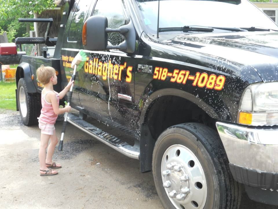 A little girl is washing a tow truck that says gallagher 's