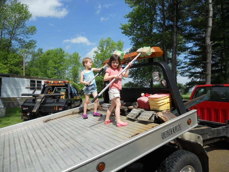 Two little girls are standing on the back of a tow truck
