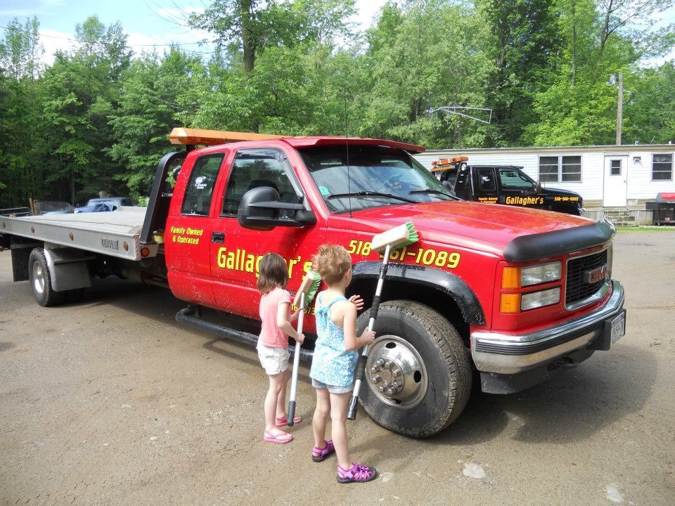 Two little girls standing next to a red tow truck that says gallard