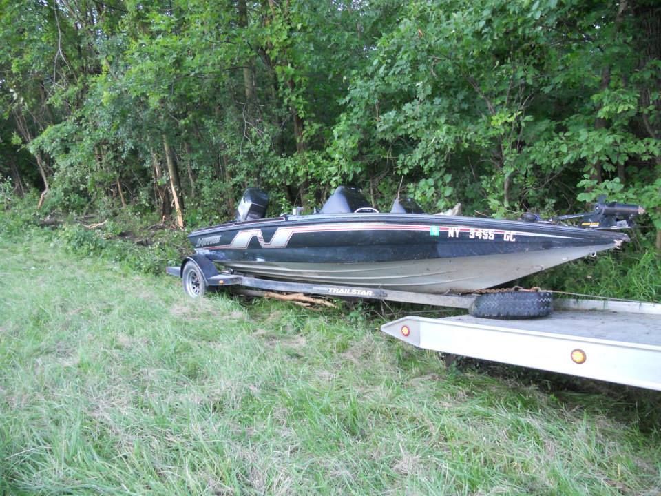 A fishing boat is sitting on top of a trailer in a grassy field.