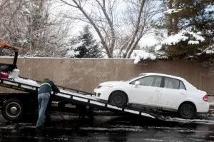 A white car is being towed by a tow truck.