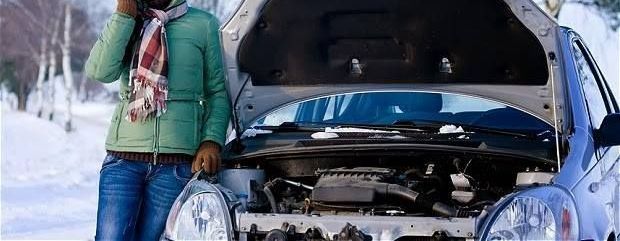 A woman is standing next to a broken down car talking on a cell phone.