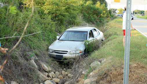 A car is stuck in a ditch on the side of the road.
