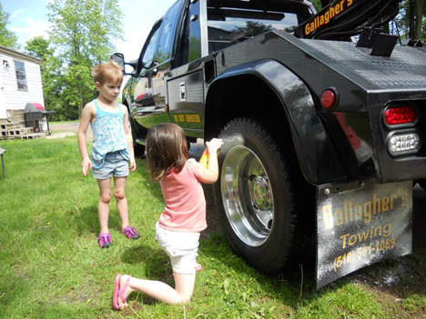 Two little girls are kneeling in front of a tow truck.