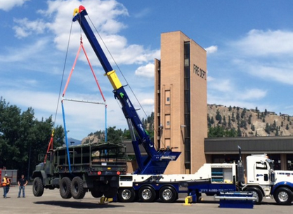 A military truck is being lifted by a crane in front of a building that says peters