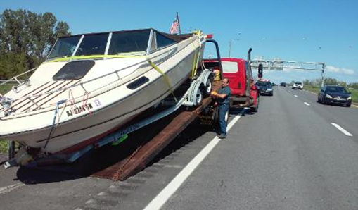 A boat is being towed down a highway by a tow truck.