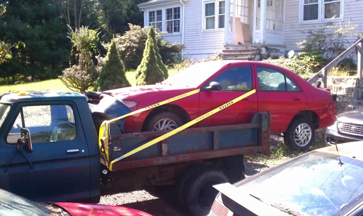 A red car is being towed by a tow truck