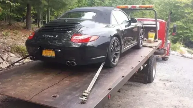 A black car is sitting on top of a tow truck.