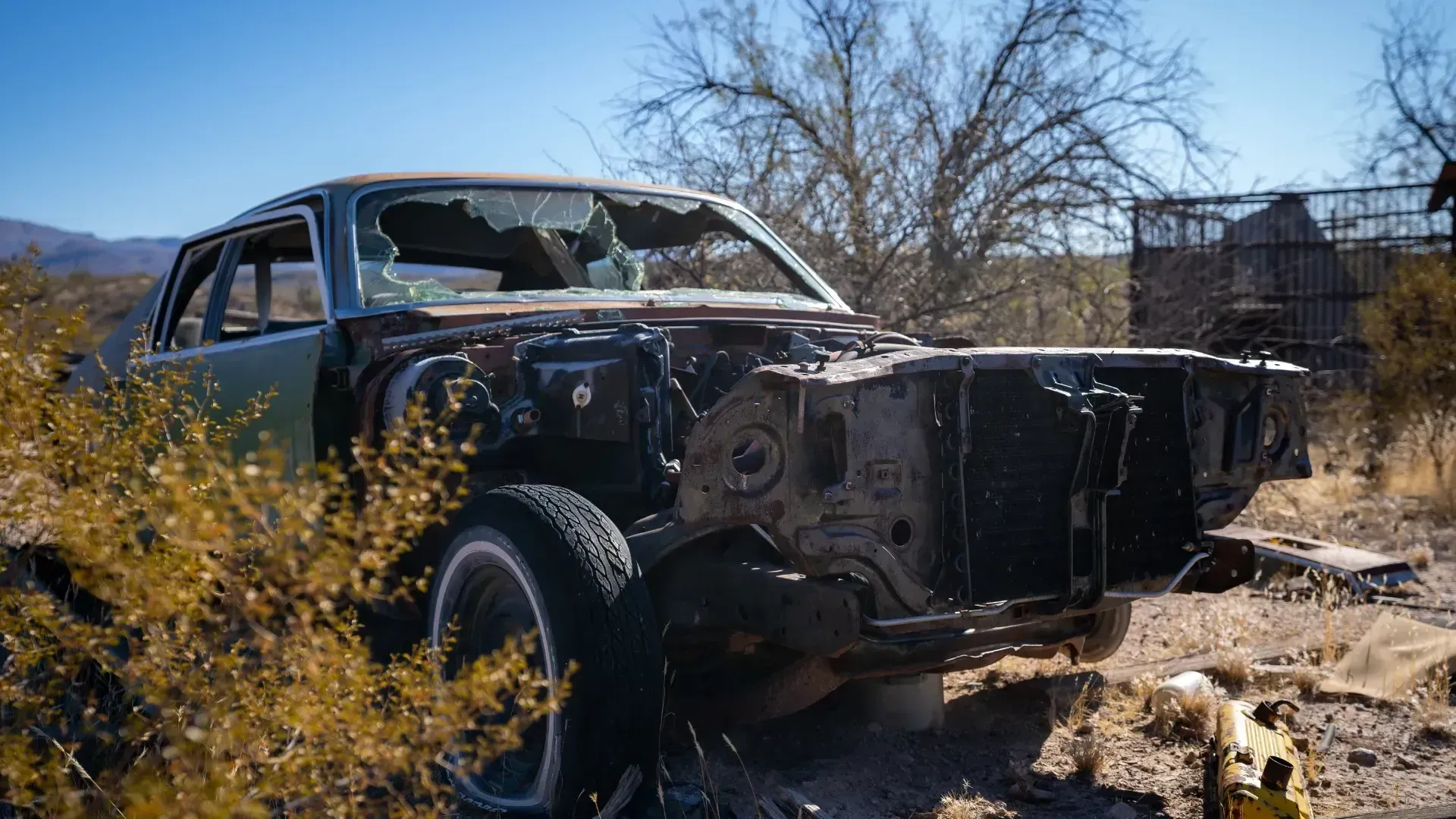 A broken down car is sitting in the middle of a desert.
