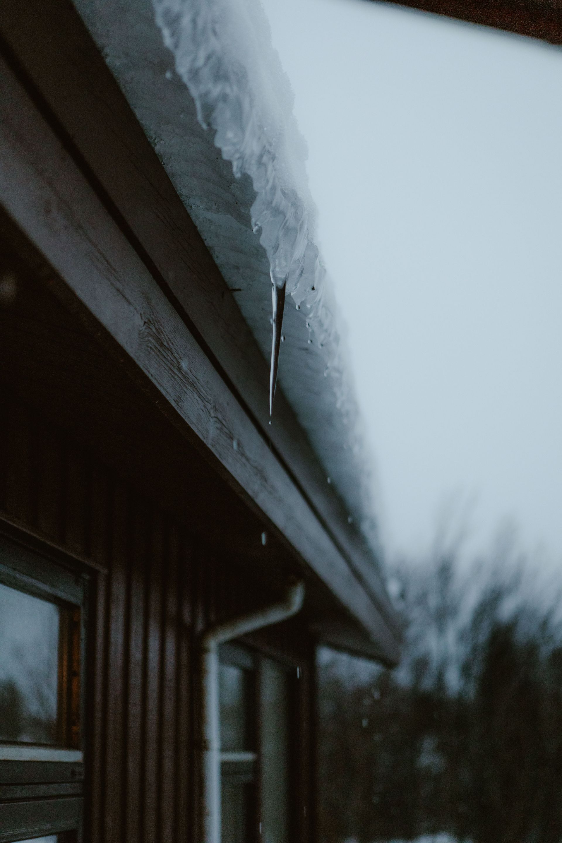 Icicles hanging from a snow-covered roof edge above a house window