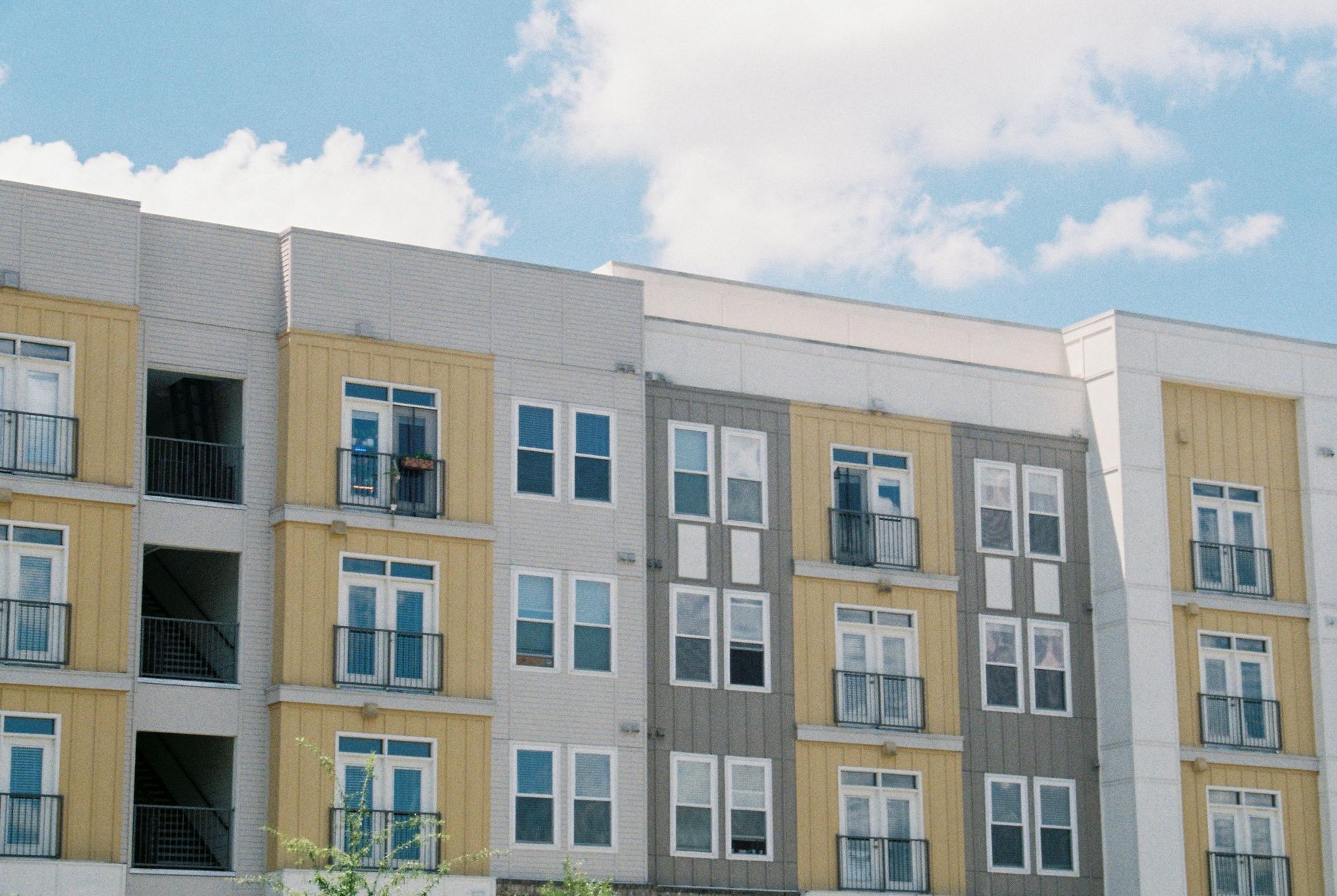 Modern apartment building facade with gray, white, and beige panels under a blue sky