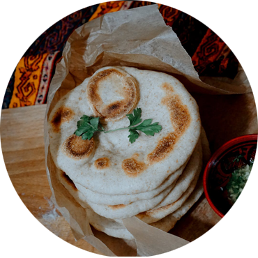 Stack of flatbread in a paper bag, garnished with parsley, next to a small bowl of sauce.