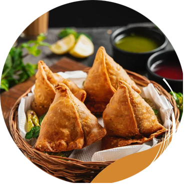 Basket of golden samosas with dipping sauces and lemon slices.