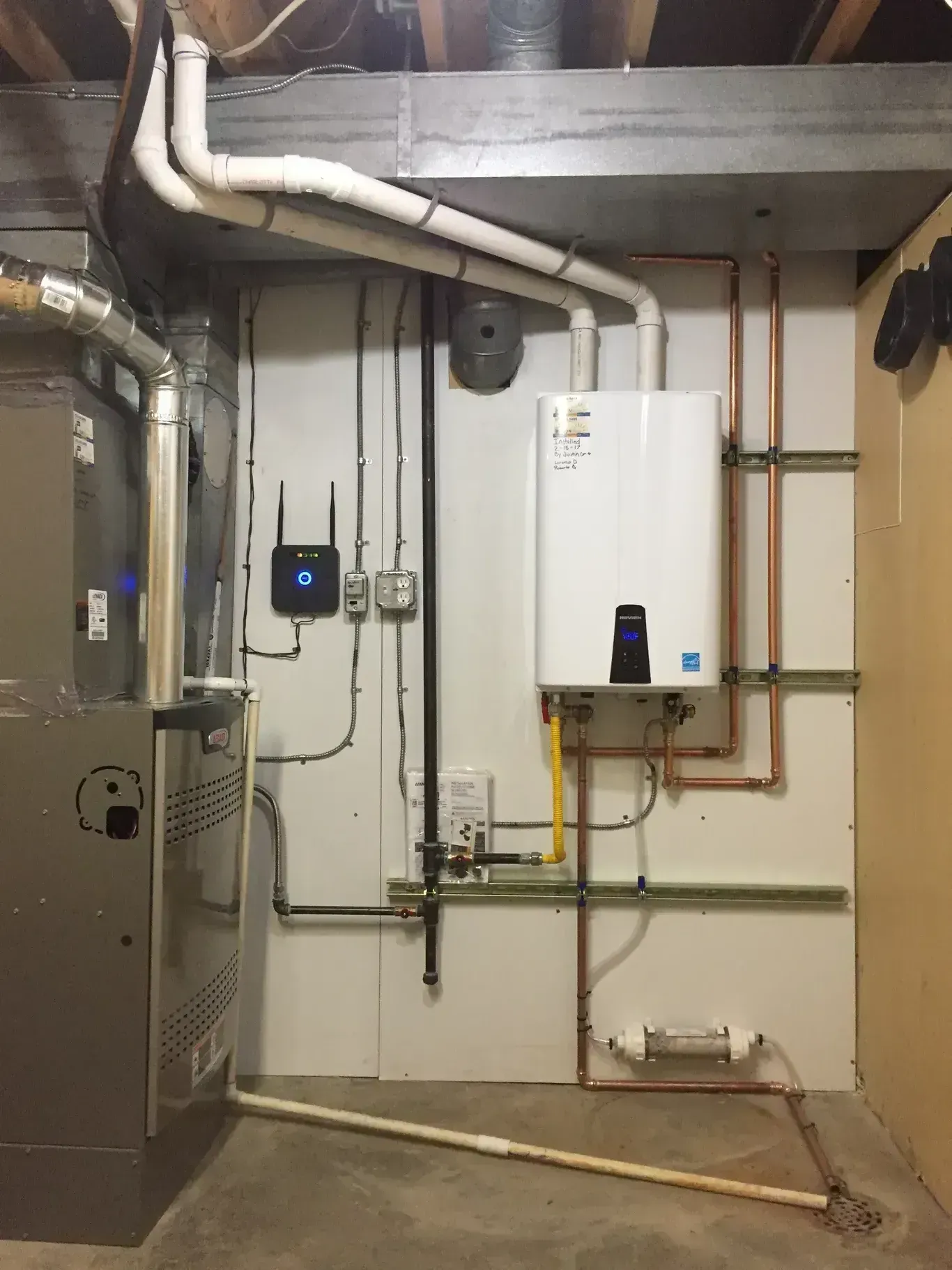 Water heater and furnace with pipes and wiring on a wall in a basement.