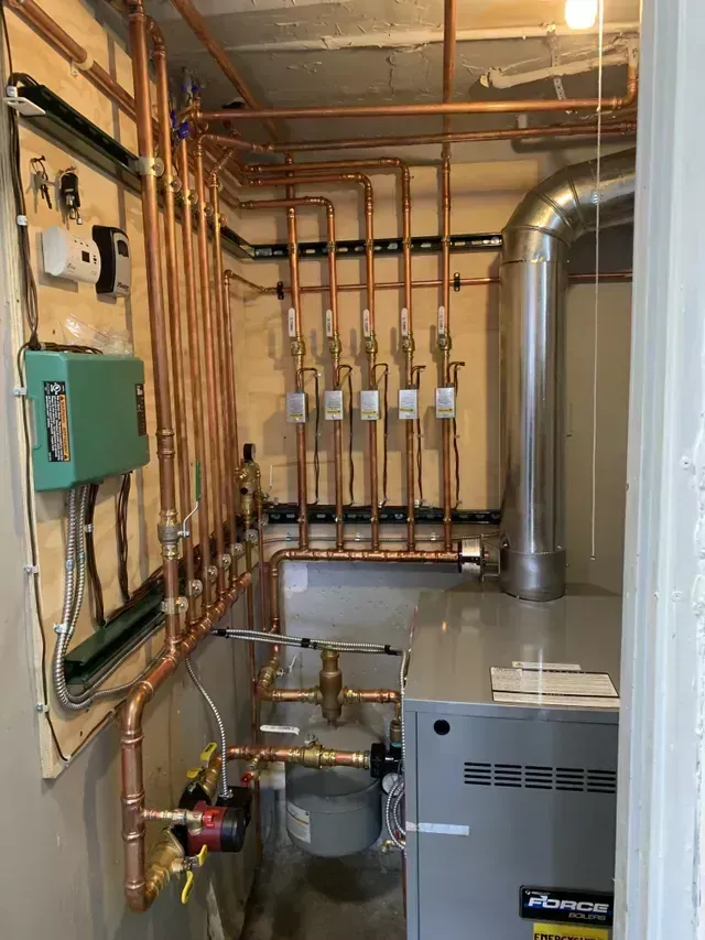 Copper pipes and furnace in a utility room. Pipes are installed on wooden paneling.