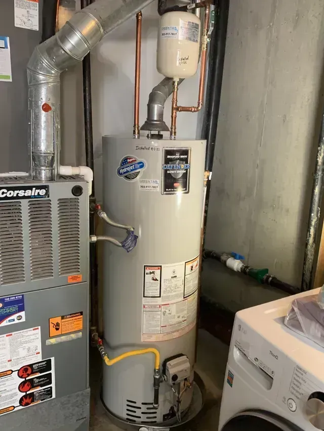 Water heater and furnace in a utility room. Gray, metallic, and white appliances with pipes.