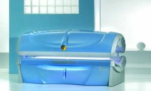 Blue tanning bed in a light-blue room, with a decorative window in the background.
