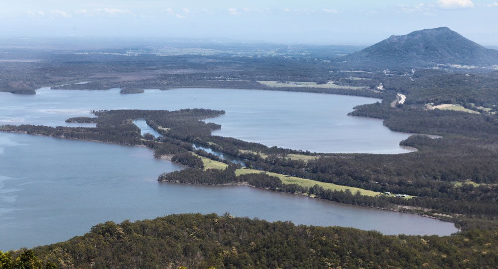 An Aerial view of a lake Surrounded by Trees and a Mountain — Unique by Nature Allied Health Service in Narangba, QLD