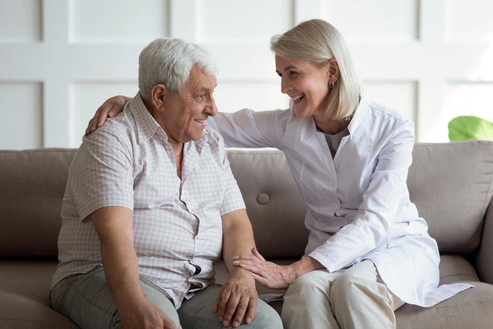 A Nurse Is Sitting On A Couch With An Elderly Man — Unique By Nature Allied Health Service In Caboolture, QLD