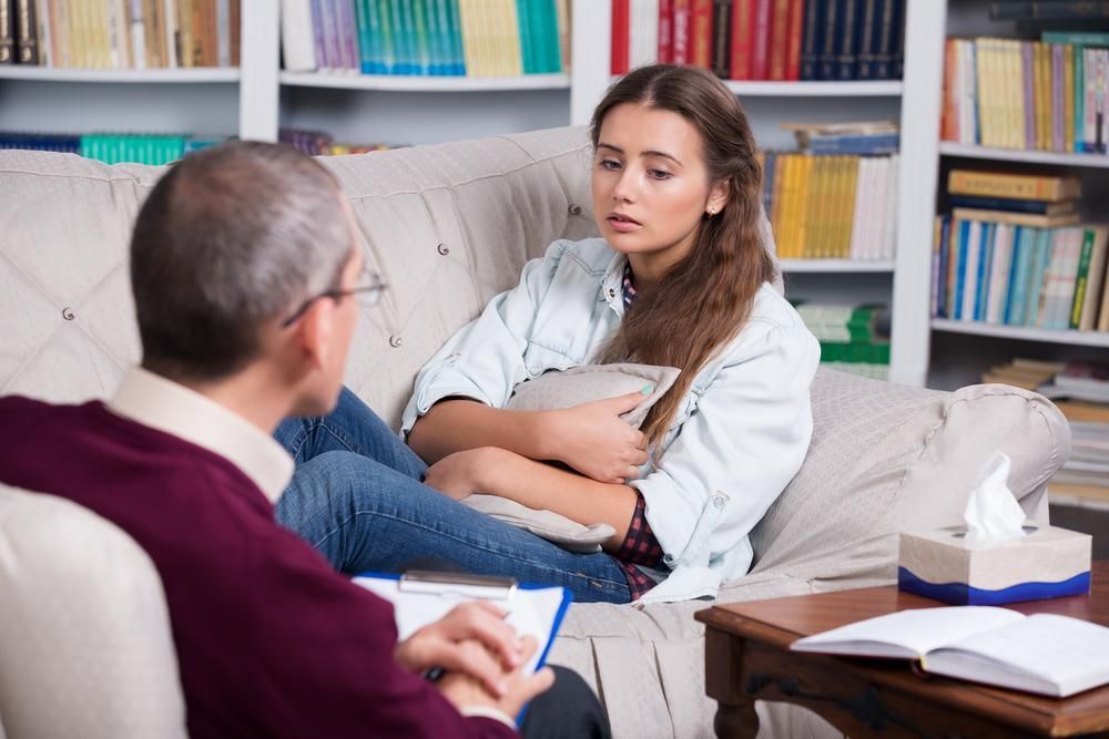 A Woman Is Sitting On A Couch Talking To A Man — Unique By Nature Allied Health Service In Burpengary, QLD