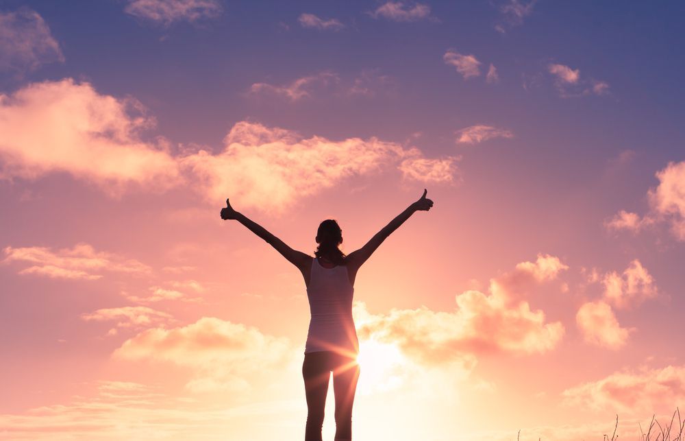 A Woman Is Standing In Front Of A Sunset With Her Arms Outstretched — Unique By Nature Allied Health Service In Burpengary, QLD