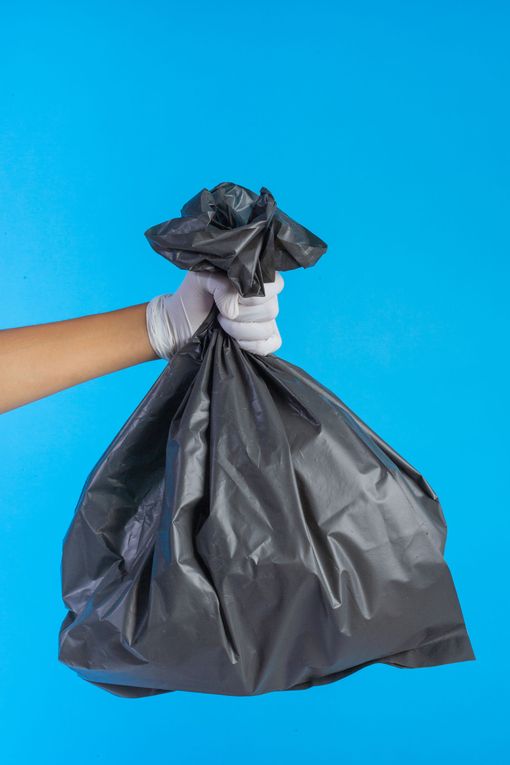 Una persona con guantes blancos sostiene una bolsa de basura negra sobre un fondo azul.