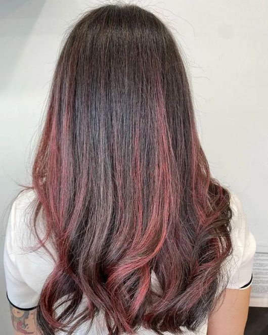 Lunghi capelli mossi castano scuro con riflessi rosa, visti di spalle su uno sfondo chiaro.