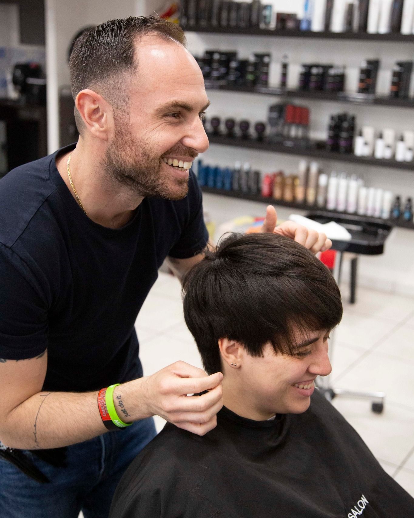 Una parrucchiera sorride mentre taglia i capelli scuri di una cliente in un salone.