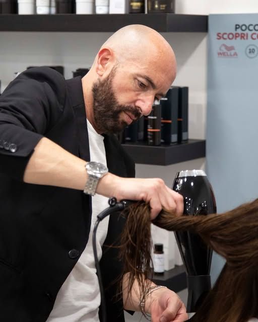 Un parrucchiere asciuga con il phon i capelli castani di una cliente in un salone.