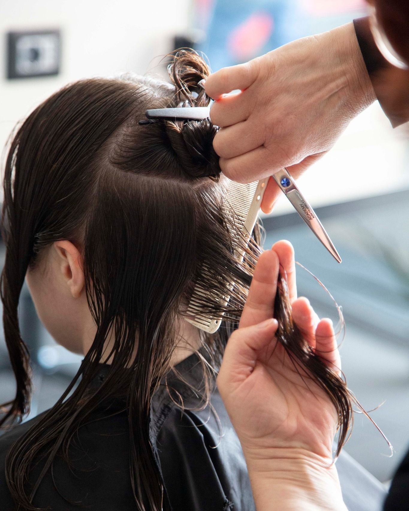 Un parrucchiere taglia con le forbici i capelli scuri di una cliente in un salone.