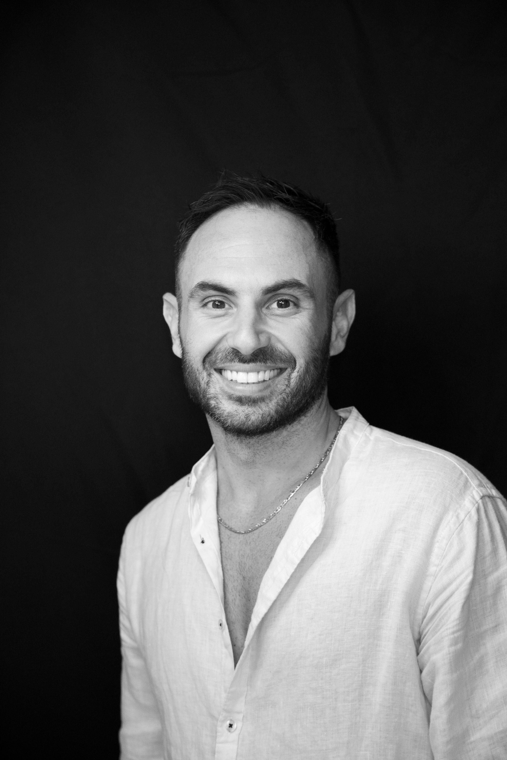 Uomo sorridente con camicia bianca su sfondo scuro.