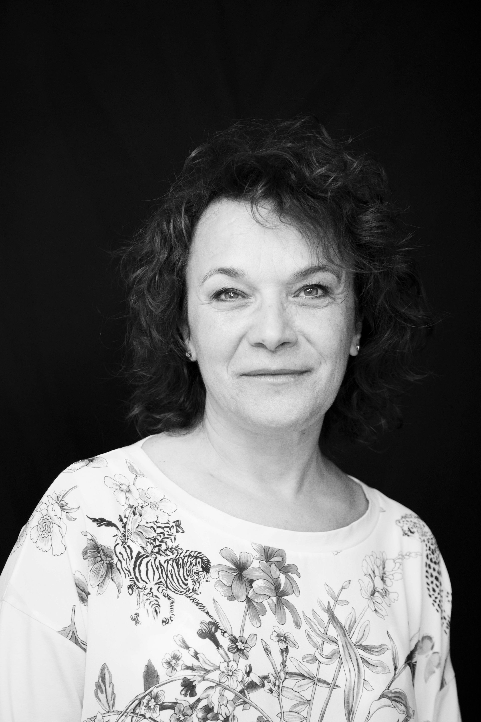 Ritratto di una donna con una blusa a fiori su sfondo scuro, che guarda in camera con un leggero sorriso.