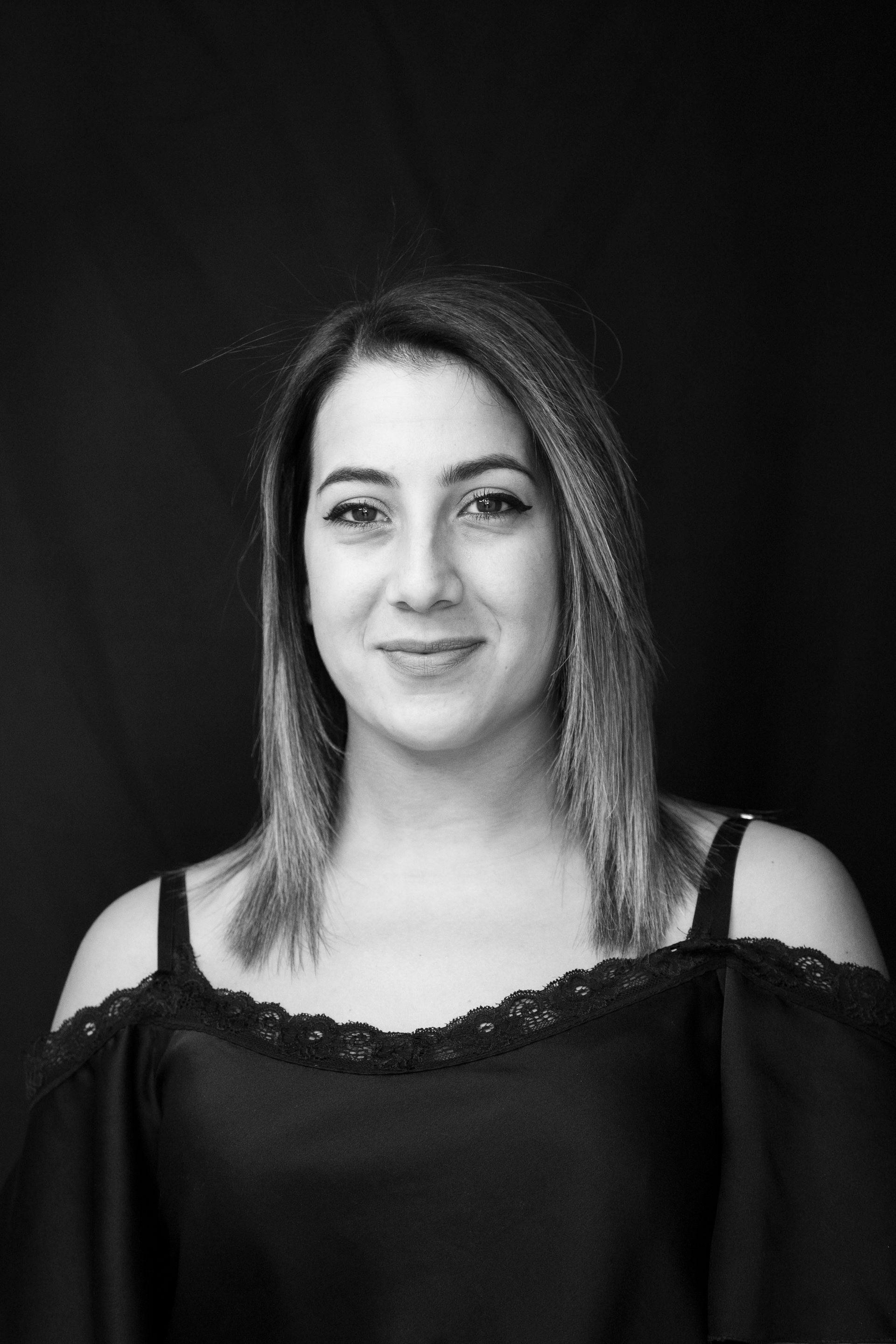 Ritratto in bianco e nero di una persona sorridente con un top scuro a spalle scoperte su sfondo nero.