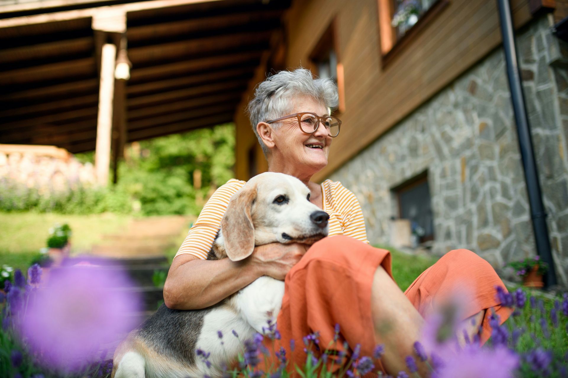 An elderly woman is sitting on the ground holding a dog.