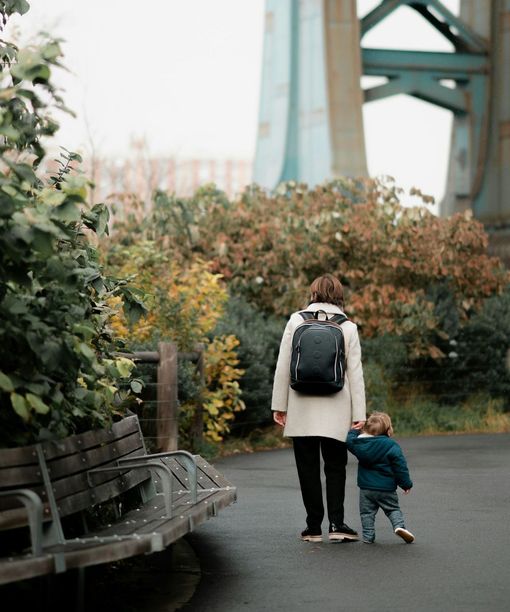 A woman with a backpack is walking with a child.