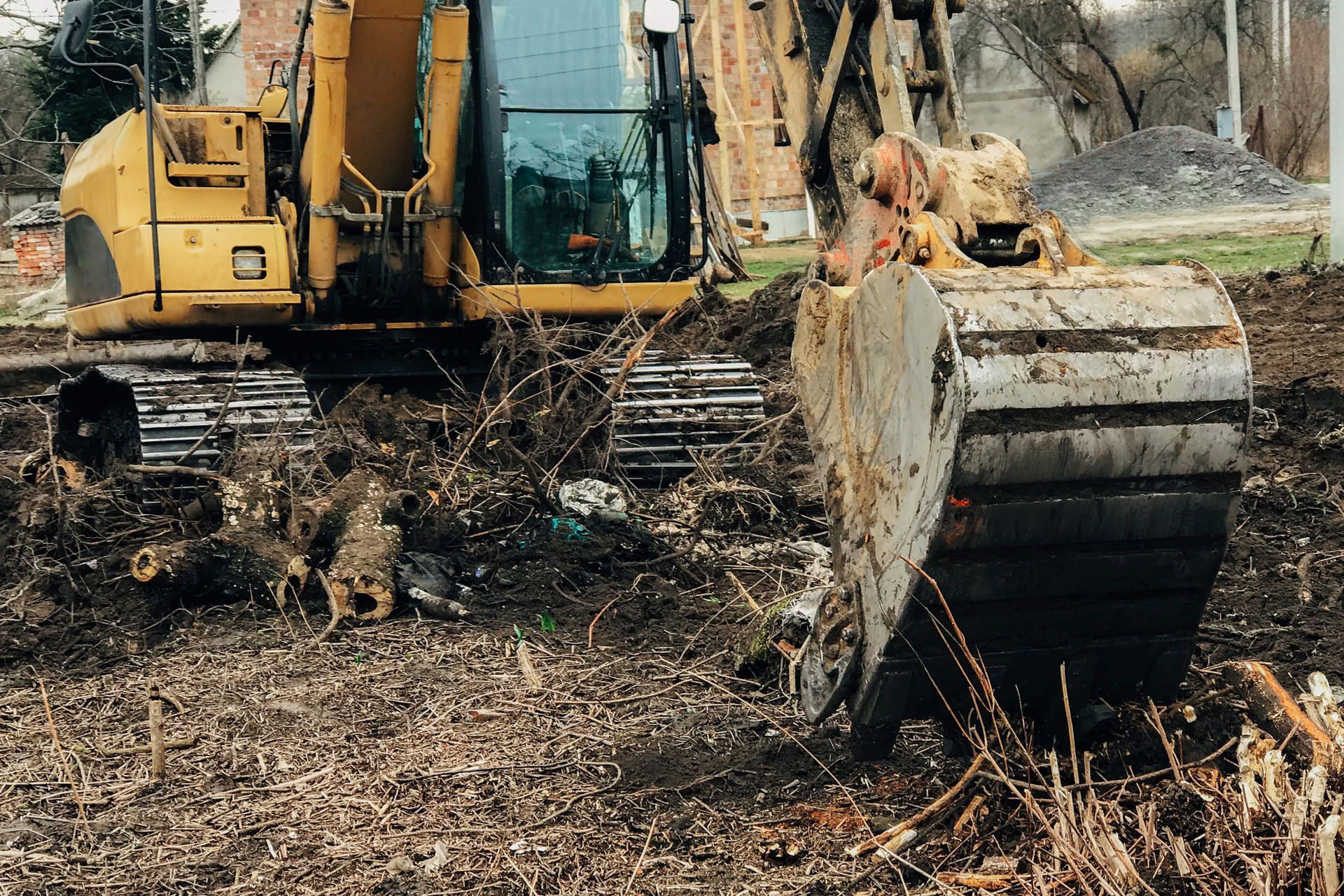 Excavator uprooting trees on land in countryside. Bulldozer clearing land from old trees, roots and branches with dirt and trash. Backhoe machinery. Yard work