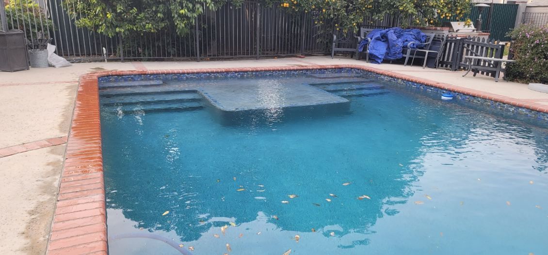 A rectangular swimming pool with blue water and a central stepped entrance platform, framed by a red brick border.