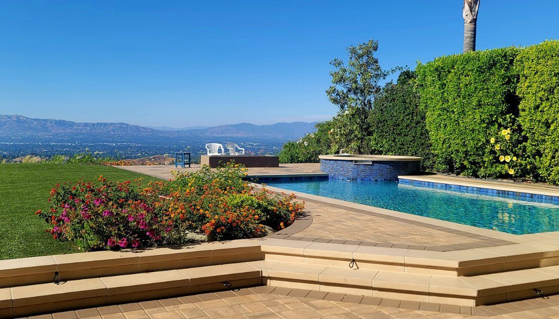 A backyard swimming pool with a stone deck, manicured hedges, and a panoramic view of a valley and distant mountains.
