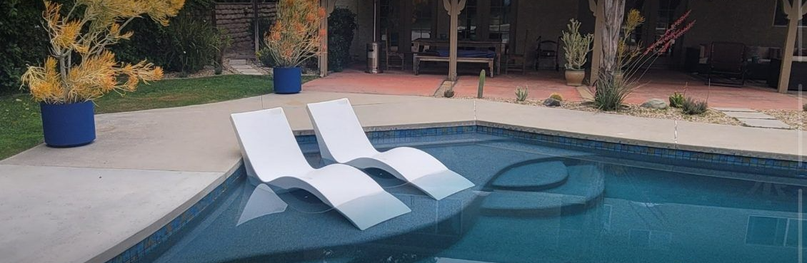 Two white lounge chairs sit partially submerged on a tanning ledge in a backyard swimming pool.
