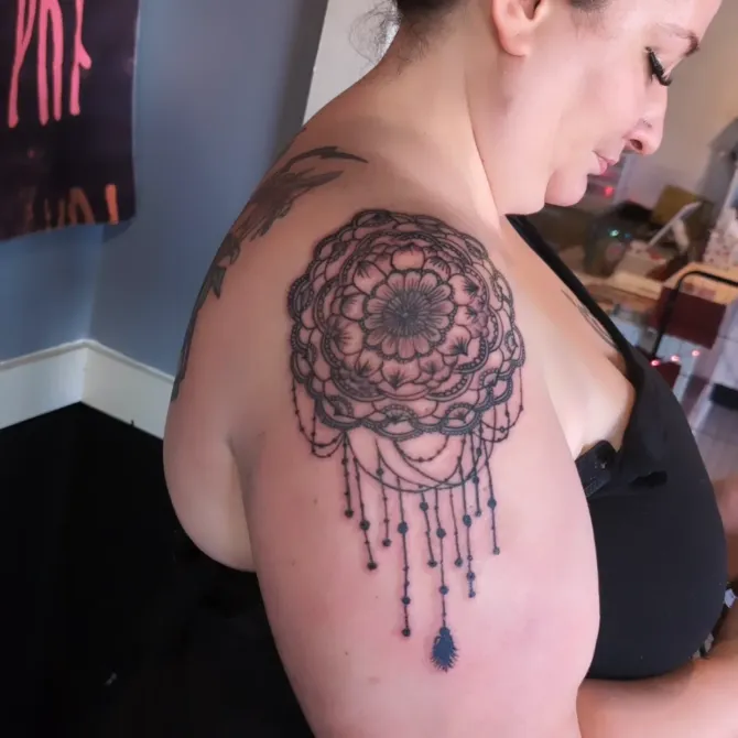 A woman has a tattoo of a dream catcher on her shoulder