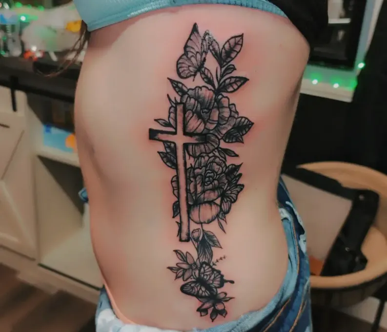 A woman has a tattoo of a cross and flowers on her side