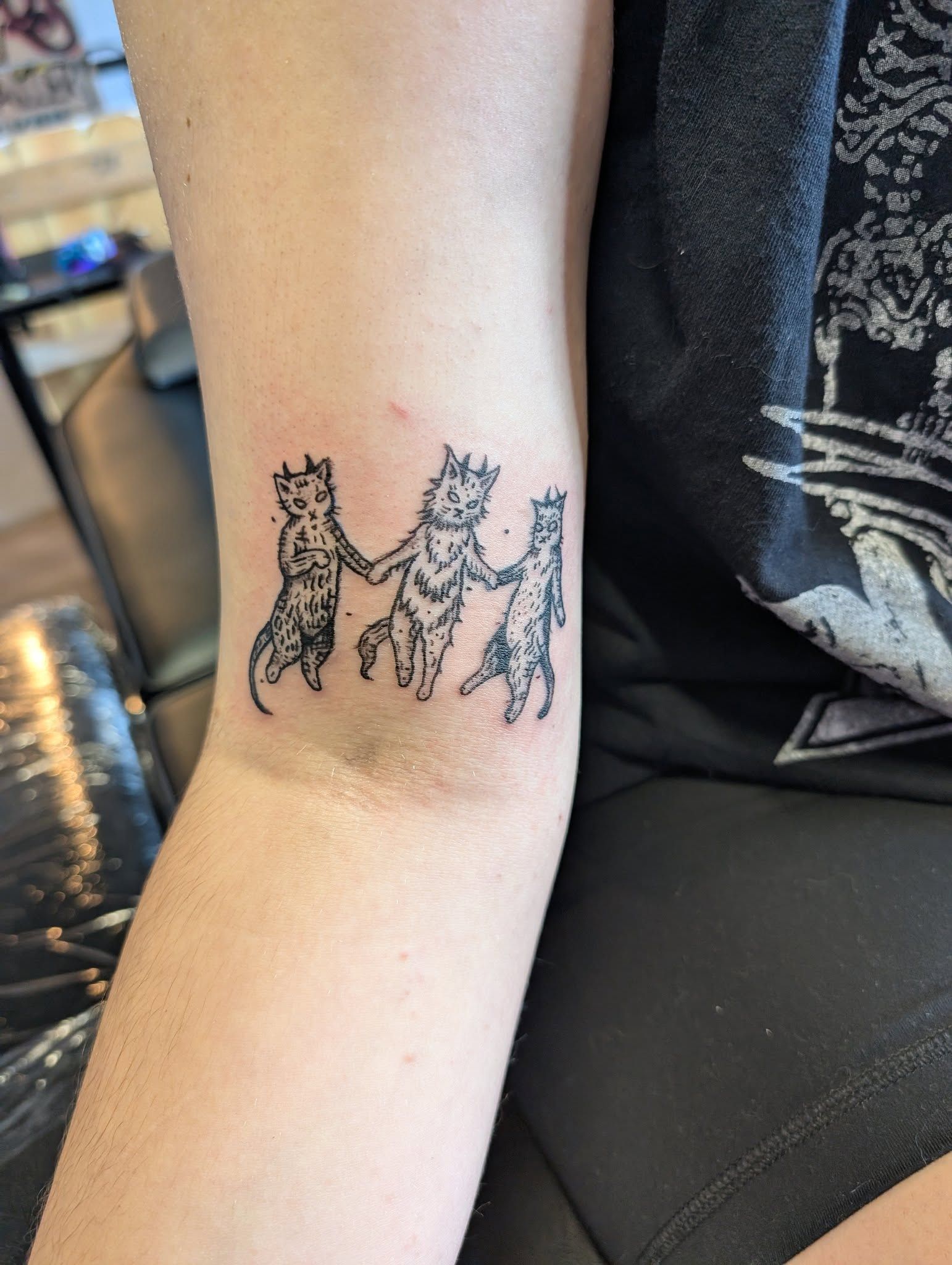 A tattoo of three cats holding hands on a person 's arm