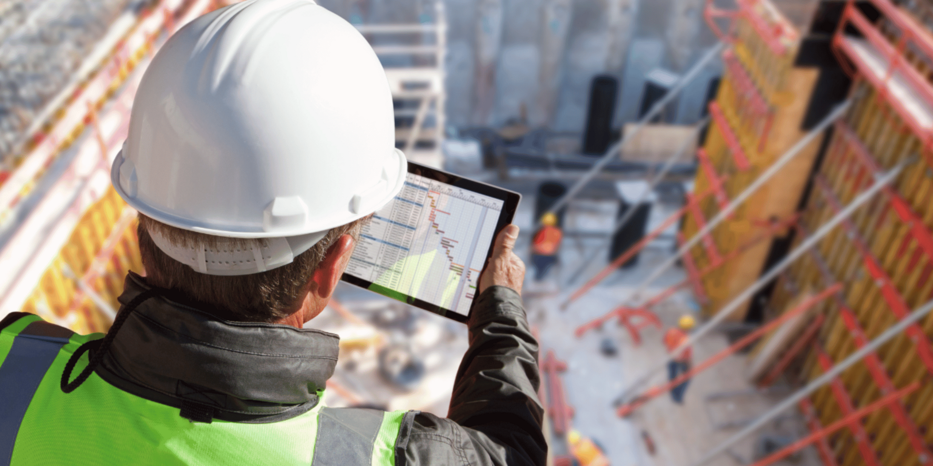 Construction worker in hard hat using tablet at a construction site.