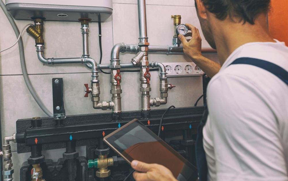 A Man Is Working On A Pipe System While Holding A Tablet — CG Plumbing & Drainage In Scone, NSW