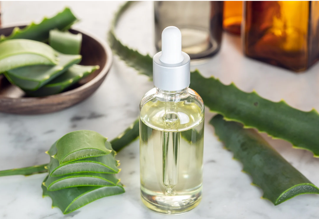 Aloe vera gel in bottle with dropper surrounded by aloe leaves.
