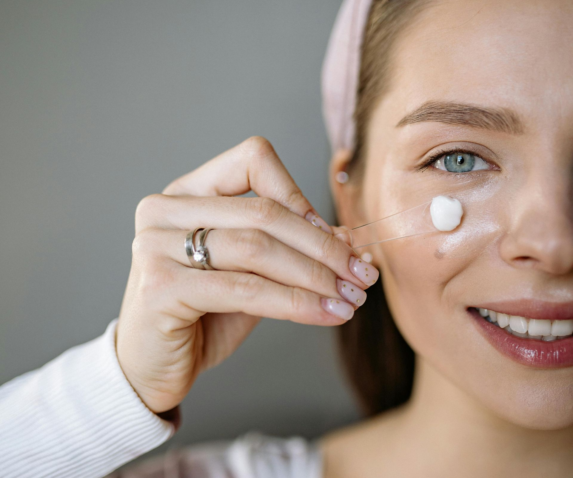 Woman applying cream to her face with a string, smiling, wearing a headband, lit setting.