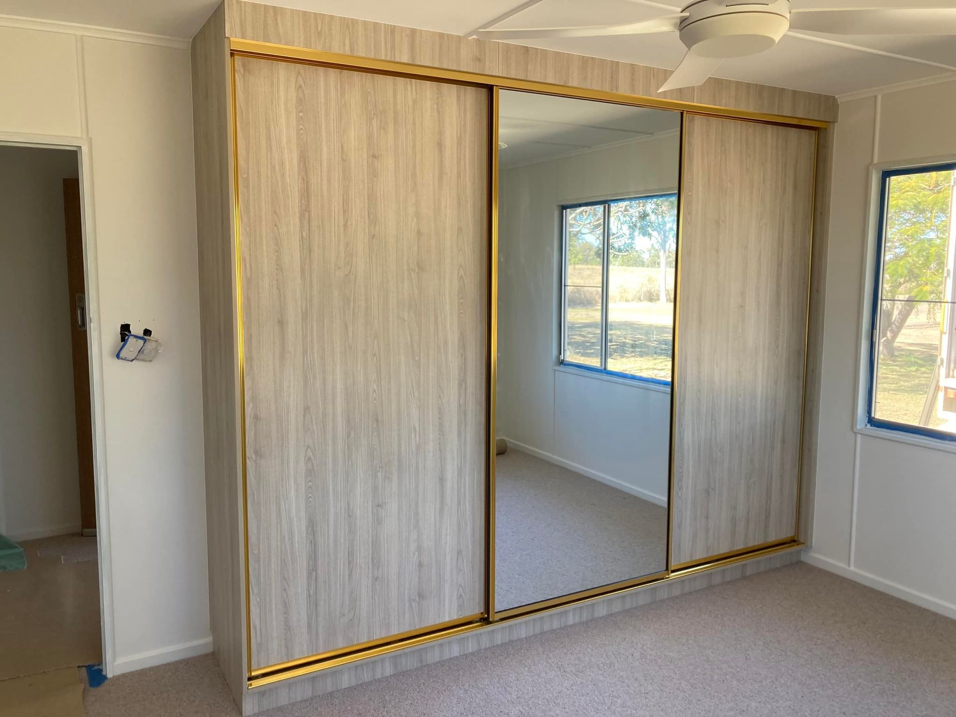Built-In Bedroom Closet with Sliding Doors, a Mirrored Center Panel, and Gold Trim; Neutral Colour Scheme — Valley Cabinetmakers In Biloela, QLD 