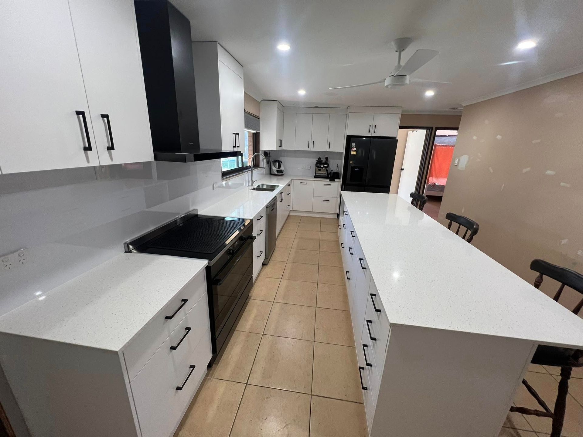 Modern kitchen with white cabinets, countertops, and a black range hood, and island with stools— Valley Cabinetmakers In Biloela, QLD 